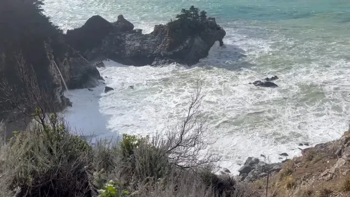 Waves breaking below coastal cliffs and a waterfall in Big Sur.