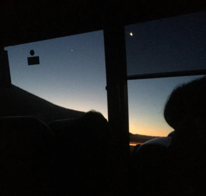 A crescent moon and sunset seen through a window.
